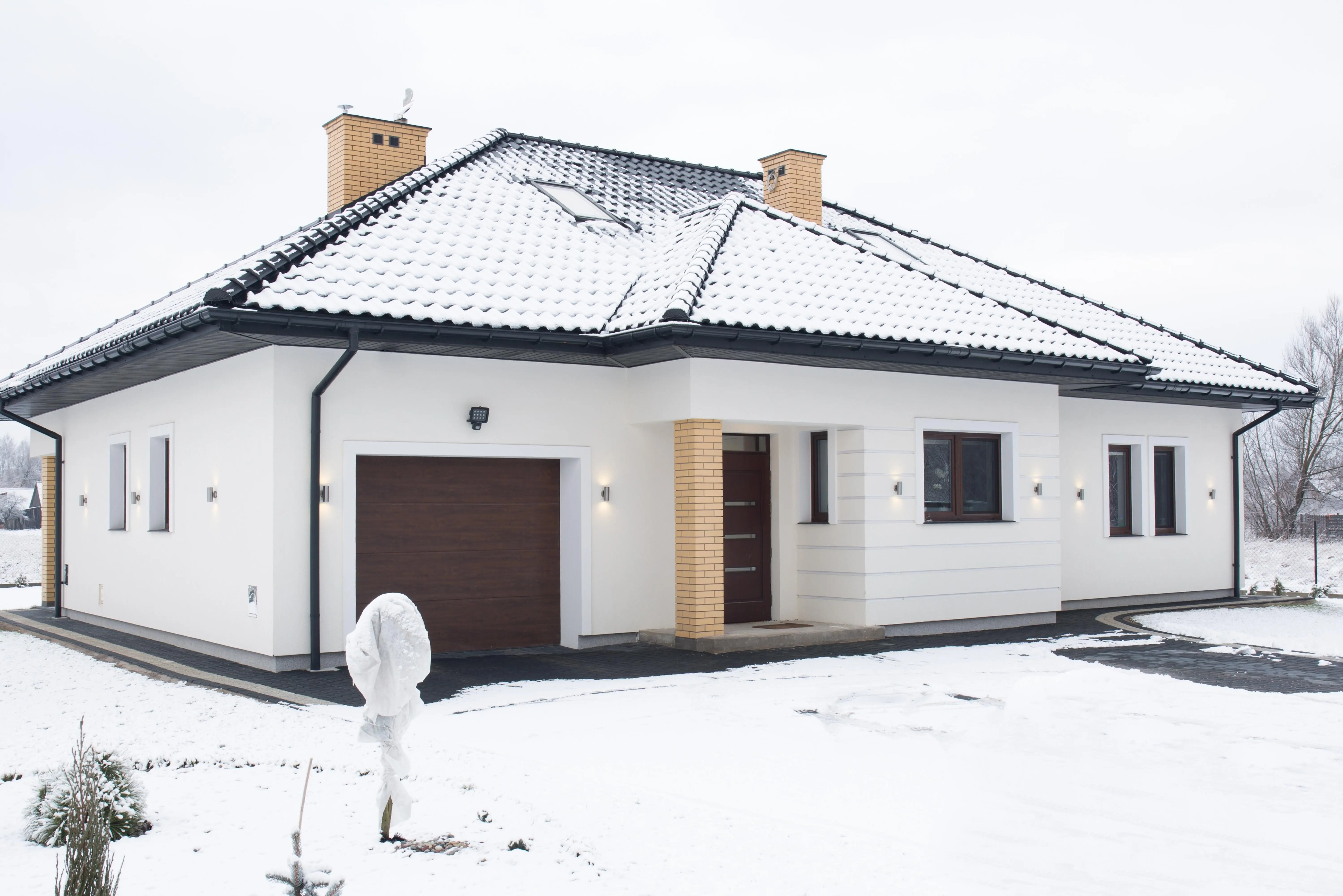 A white house with a garage and a roof covered in snow.